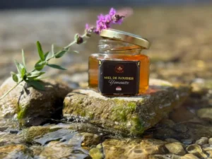 Miel de jujubier du Yémen dans pot doré posé sur pierre avec fleur violette.